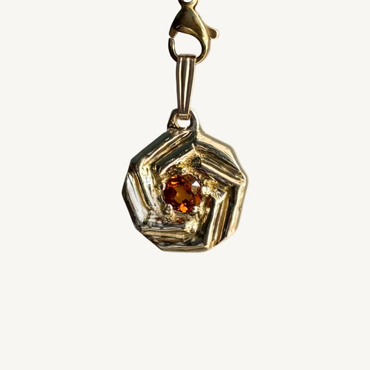 Gold pendant with a central orange gemstone on a white background